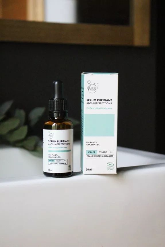 Sérum purifiant anti-imperfections Clémence & Vivien, flacon pipette brun posé sur mousse et fleurs, soin visage bio au zinc et acides naturels